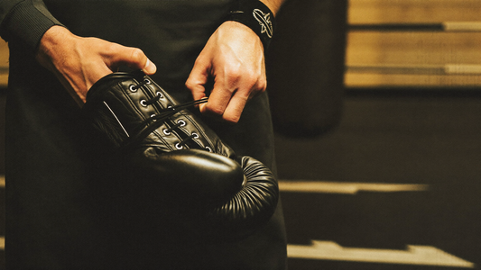 Close-up of hands lacing up black leather lace-up boxing gloves in a gym